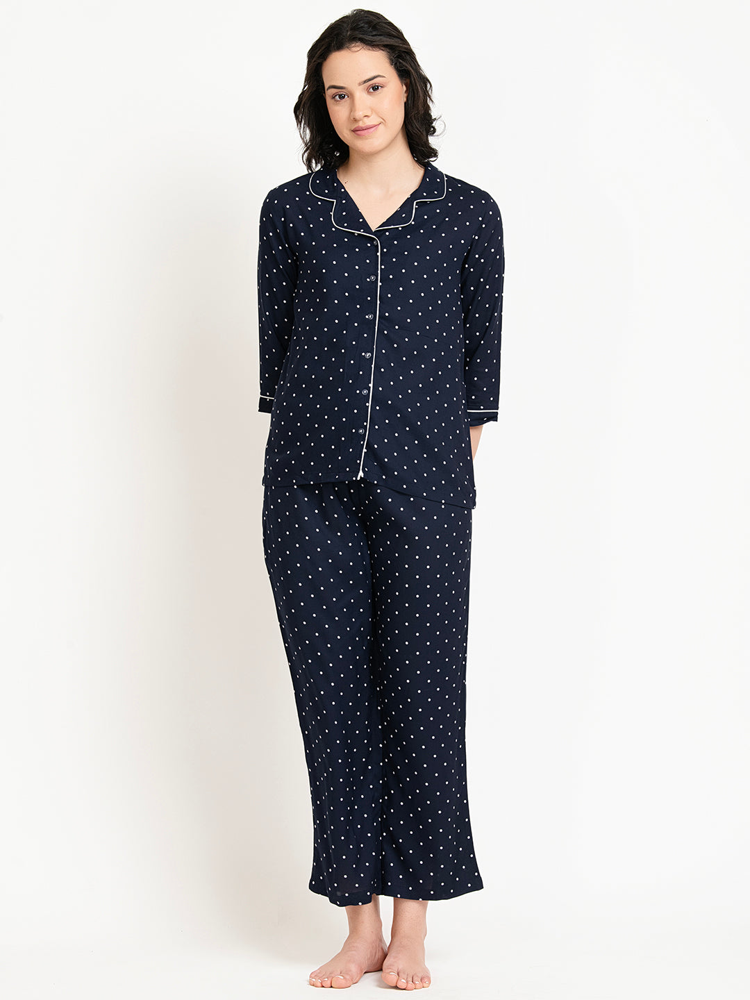 Woman wearing a navy blue pajama set with white polka dots on a white background