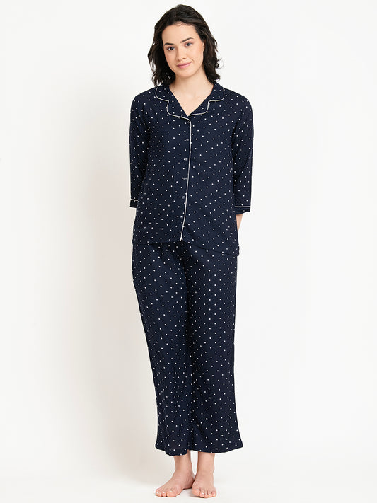 Woman wearing a navy blue pajama set with white polka dots on a white background