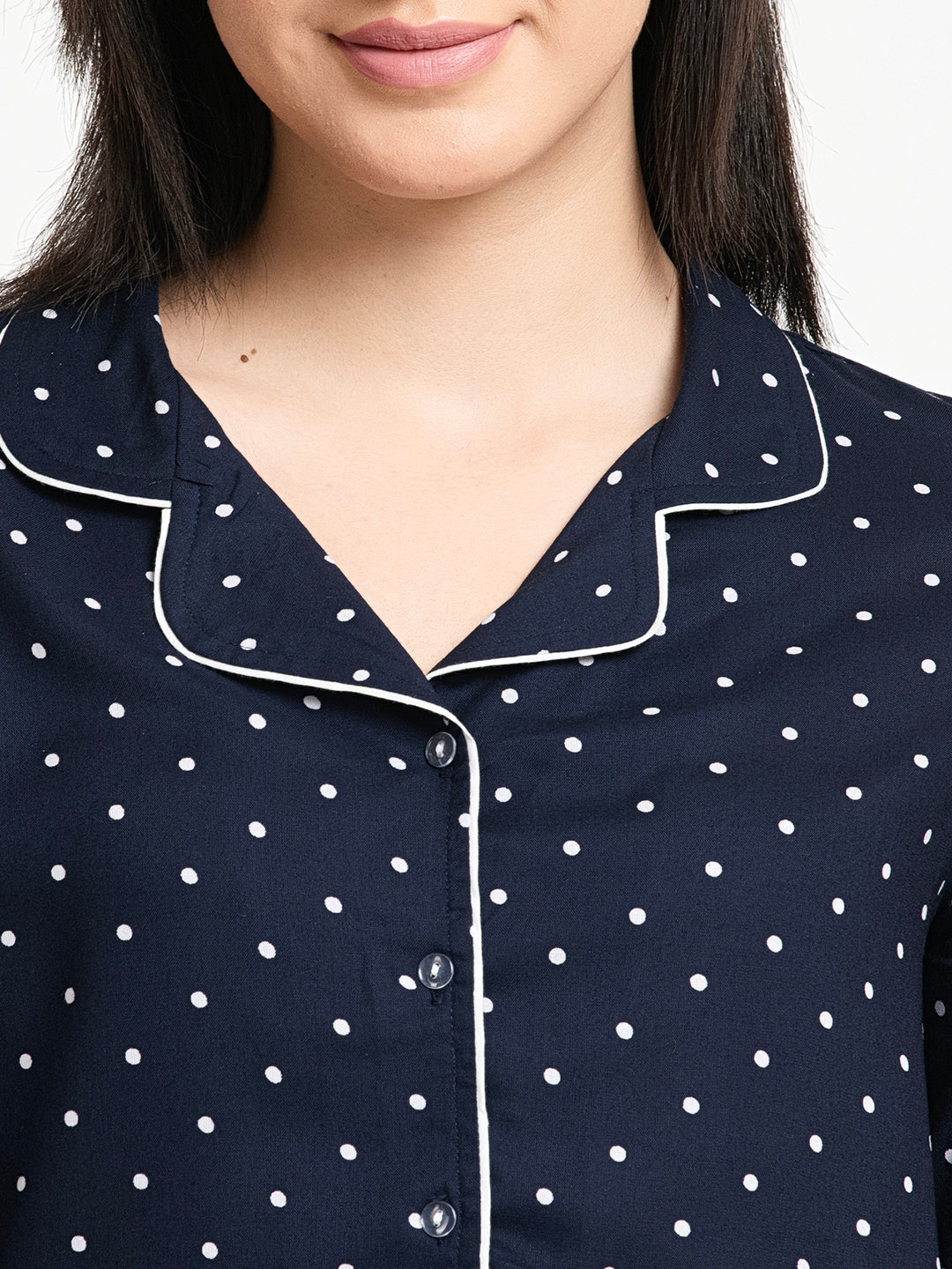Navy blue pajama top with white polka dots and trim on a plain background