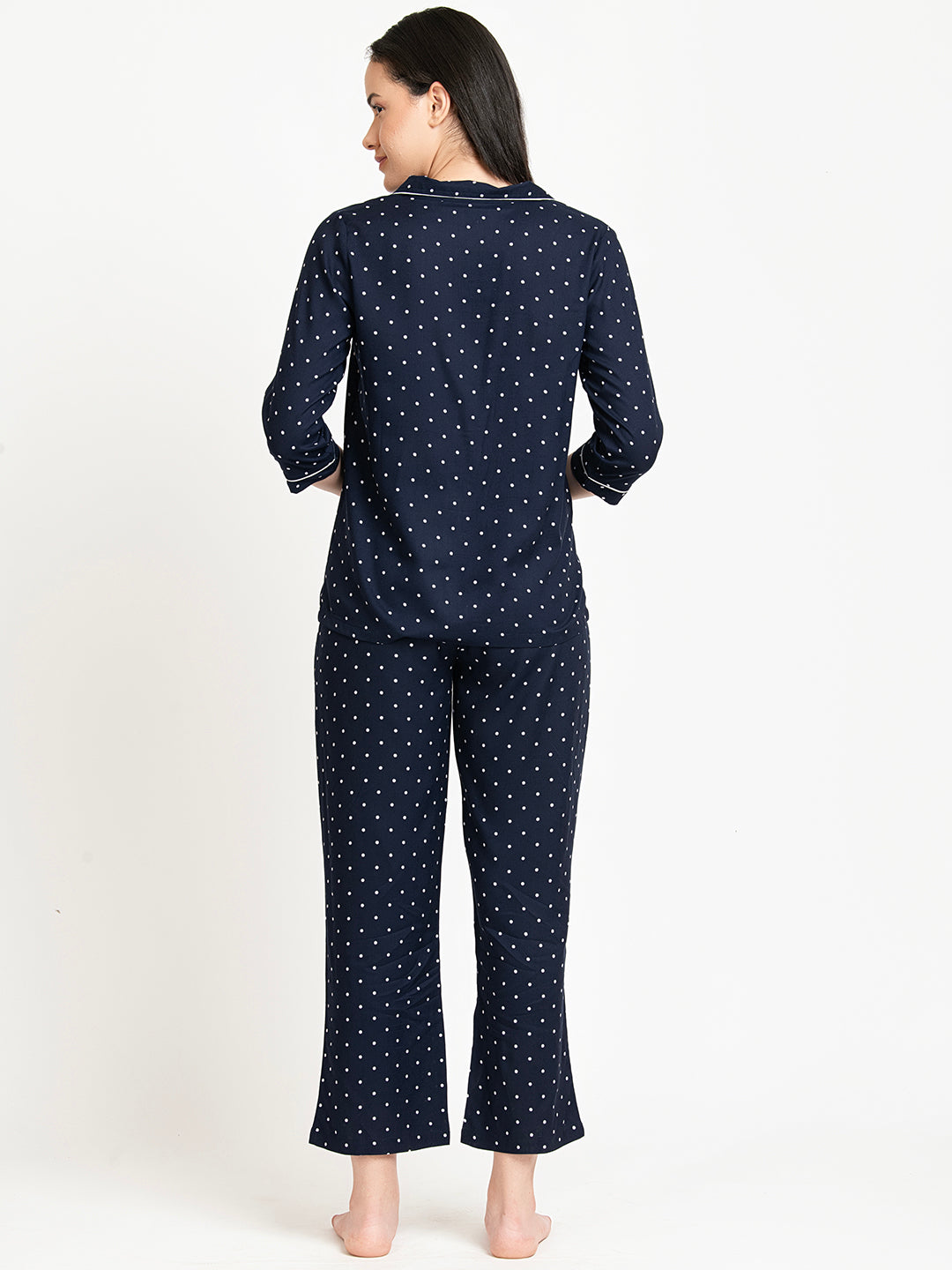 Woman wearing navy blue pajamas with white polka dots on a white background